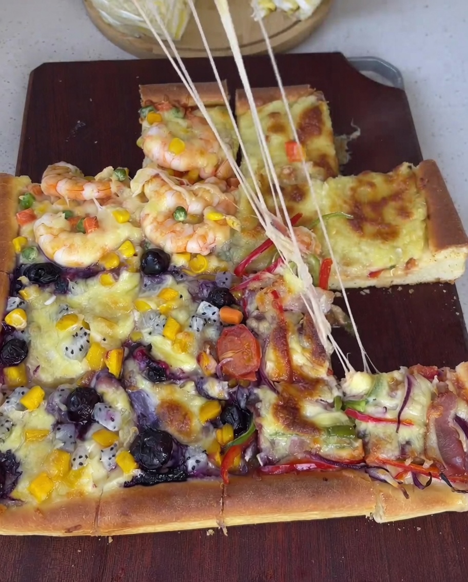 Surowe, obrane krewetki rozrzucone na części pizzy razem z groszkiem, kukurydzą i pokrojoną marchewką.