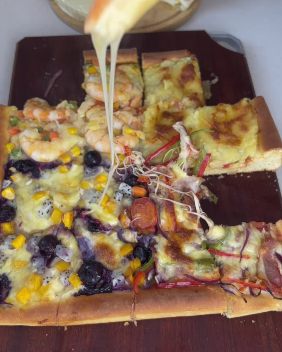 Zbliżenie na plastry boczku, czerwoną cebulę i kolorową paprykę, starannie układane na ćwiartce ciasta do pizzy.