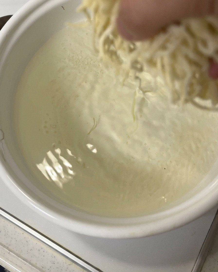 Ręka wkładająca porcję świeżego makaronu ramen do garnka z wrzącą wodą.