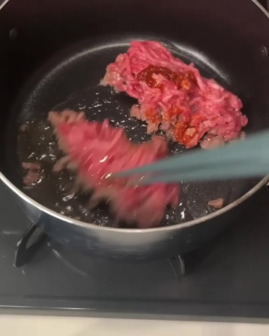 Pałeczki unoszące i mieszające kawałki mielonej wieprzowiny pokryte czerwoną pastą chili wewnątrz garnka.