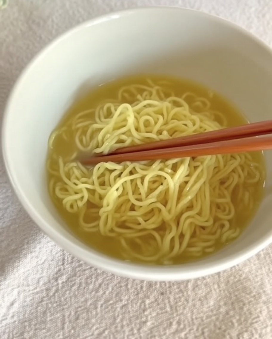 Kremowy bulion Tantanmen nalewany na gotowy makaron w misce.