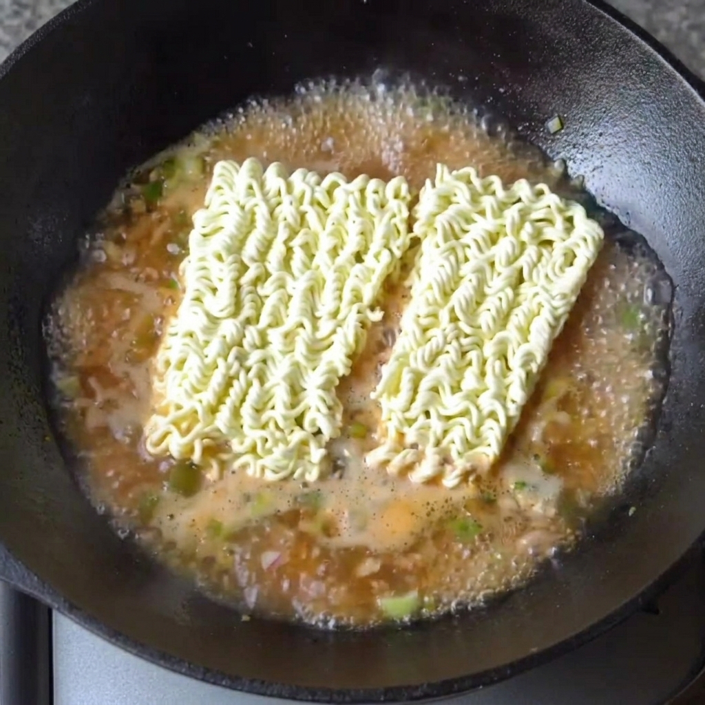 Kostki suszonego makaronu ramen spoczywające w gotującym się wywarze.