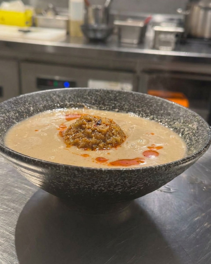 Miska japońskiego Tan Tan Ramen z kremowym bulionem, udekorowana mielonym mięsem i skropiona czerwonym olejem chili.
