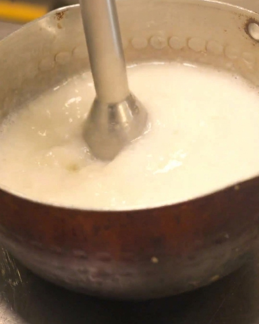 Blender ręczny tworzący kremową pianę w garnku z bulionem.