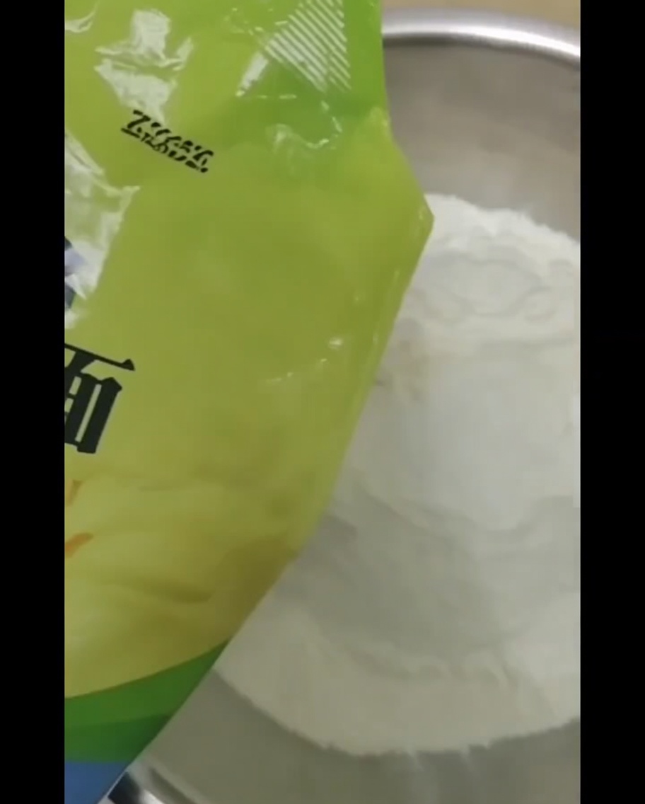 Zbliżenie na wlewanie wody do miski z mąką podczas mieszania łyżką.
