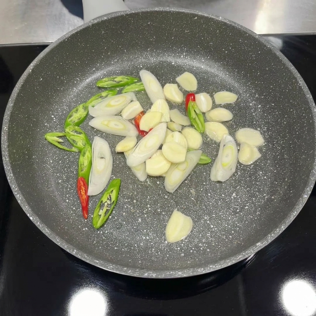 Posiekany czosnek, chili i zielona cebulka smażone na patelni aż do uwolnienia aromatu.
