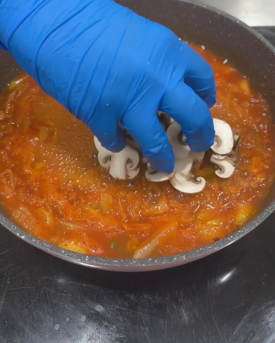 Pokrojone grzyby shiitake, cukinia i kostki tofu dodawane do wrzącej bazy zupy.