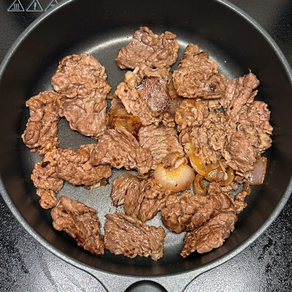 Kawałki kimchi dodawane do patelni z wołowiną i cebulą.