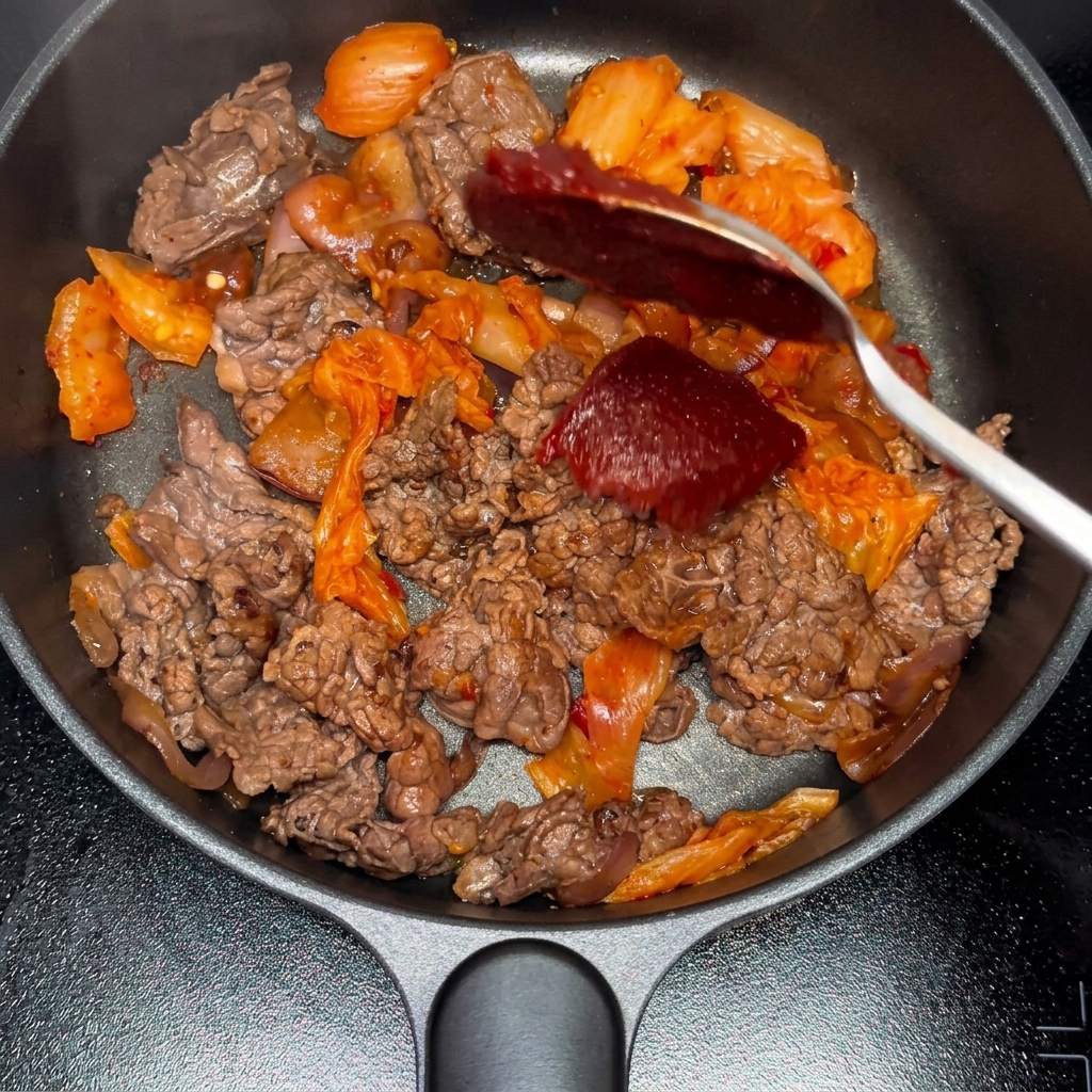 Koreańska pasta chili i proszek chili dodawane do mieszanki wołowiny i kimchi.