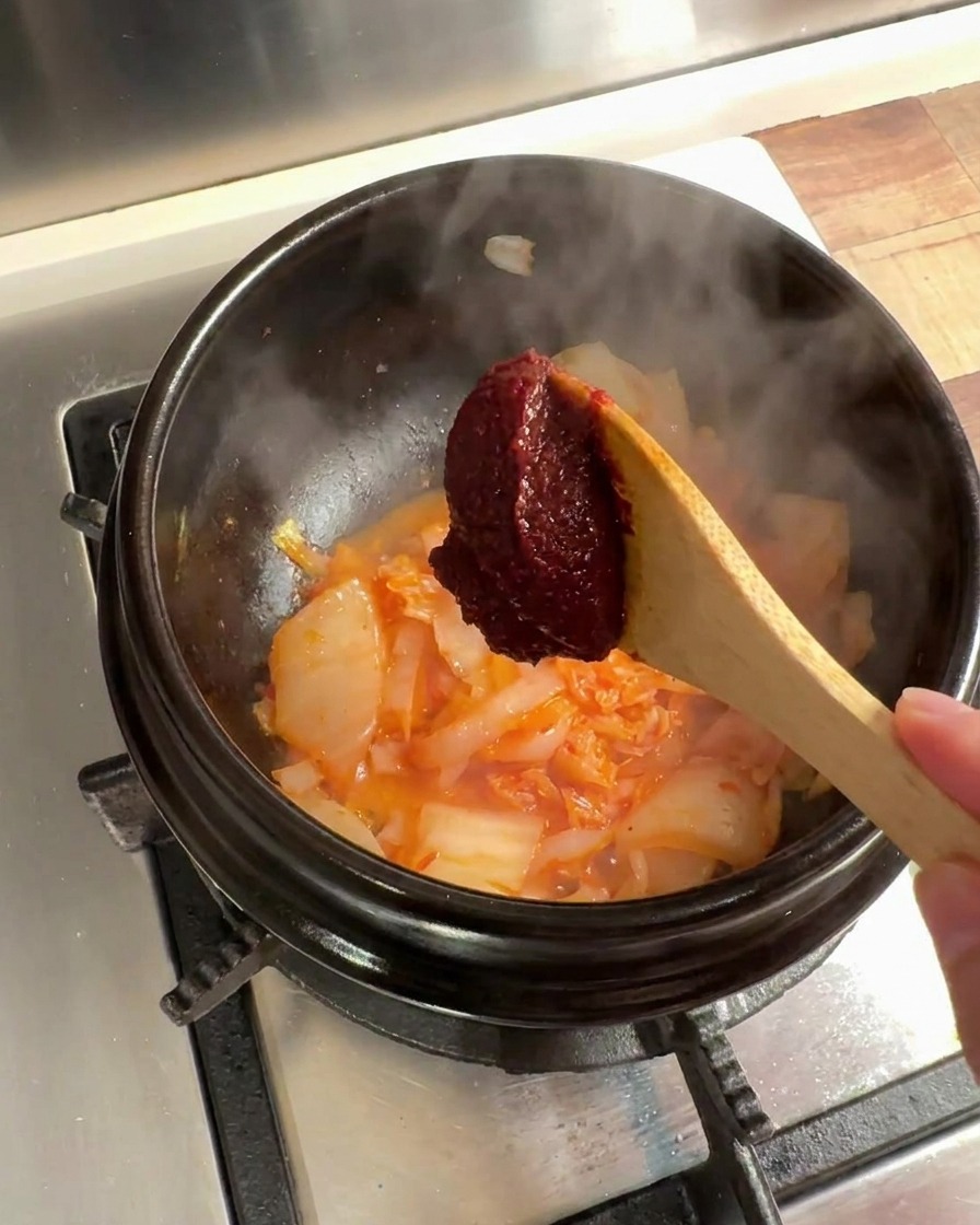 Łyżka koreańskiej pasty chili dodawana do mieszanki kimchi i cebuli w kamiennym garnku.