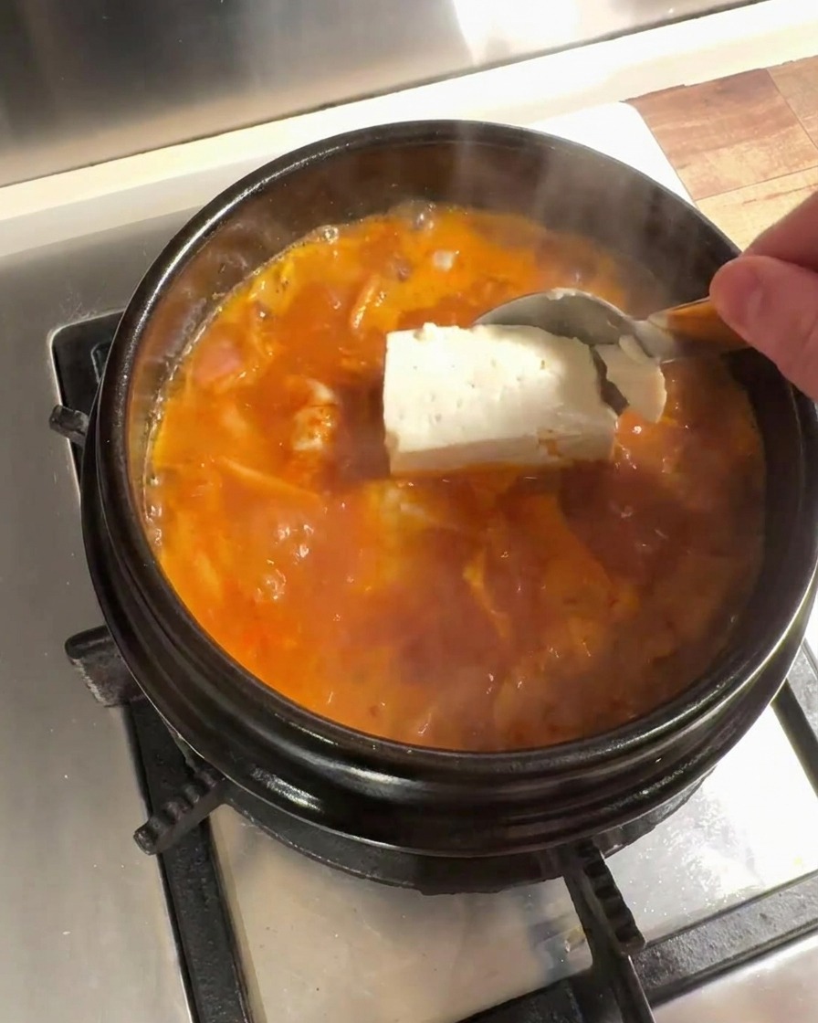 Duże kawałki świeżego tofu dodawane do gotującego się bulionu kimchi.