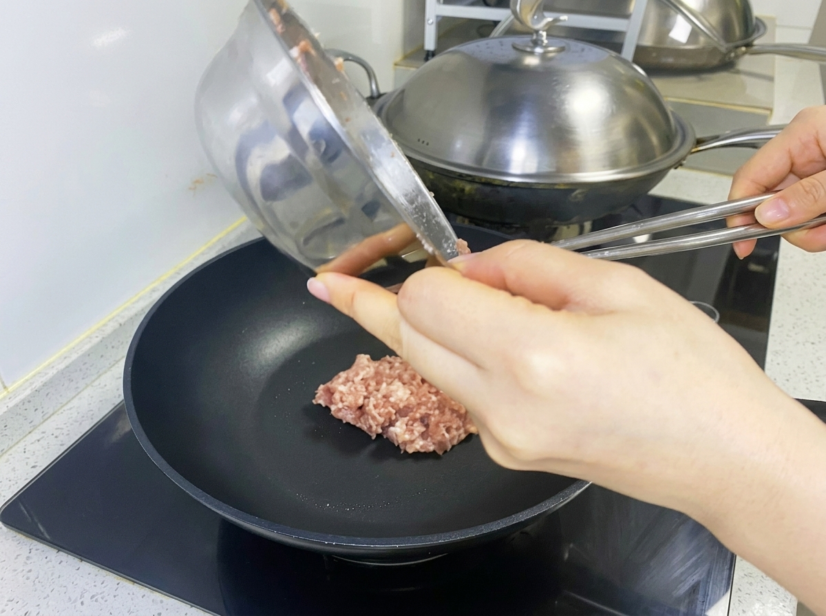 Przyprawiona mieszanka mięsna formowana w kotlet na czarnej patelni.