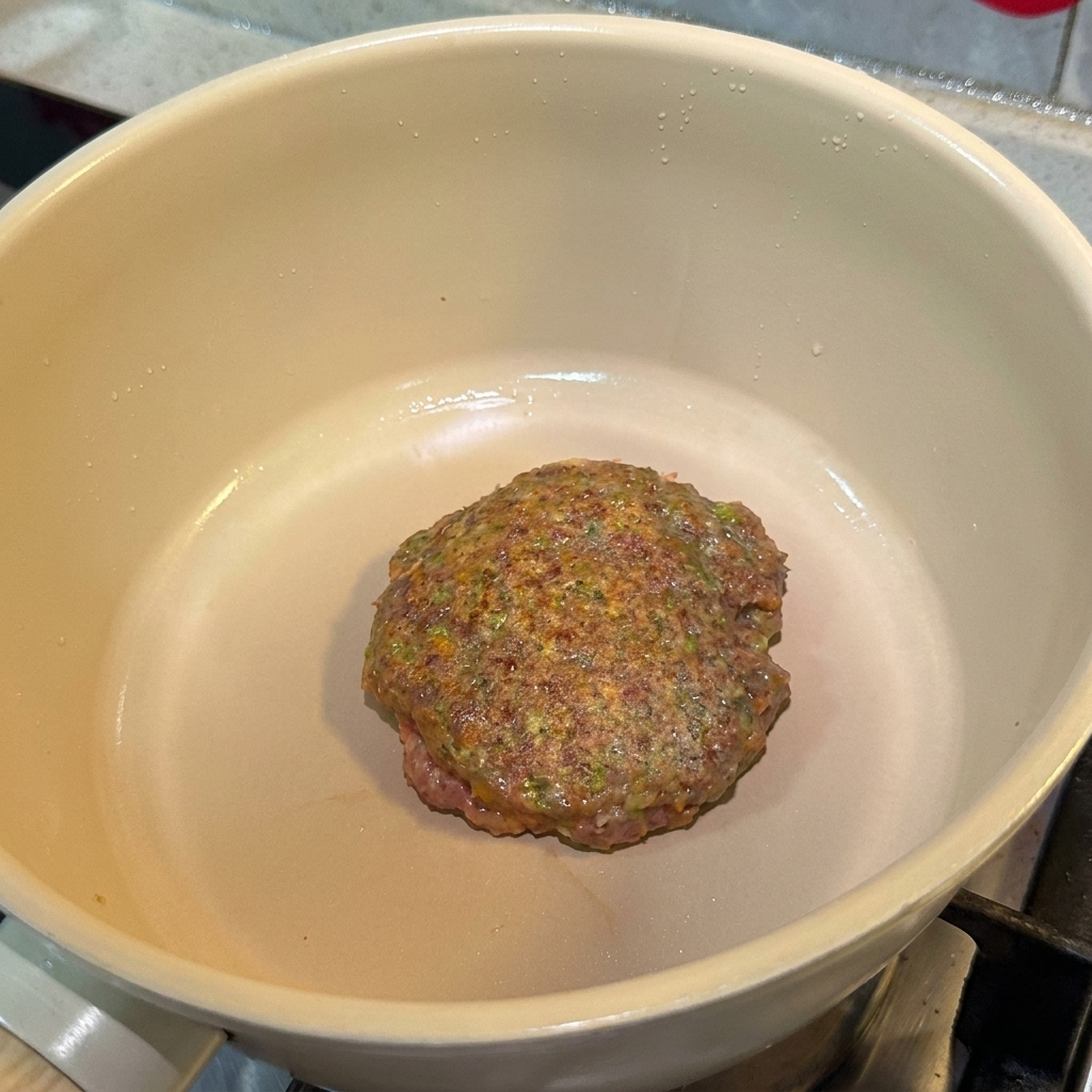 Doprawiony kotlet wołowy smażący się na patelni z zarumienioną powierzchnią.