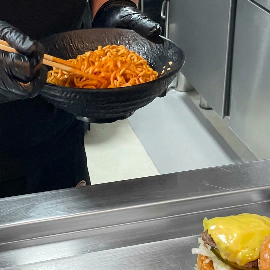 Burger z ramenem wykończony porcją makaronu i przykryty górną bułką.