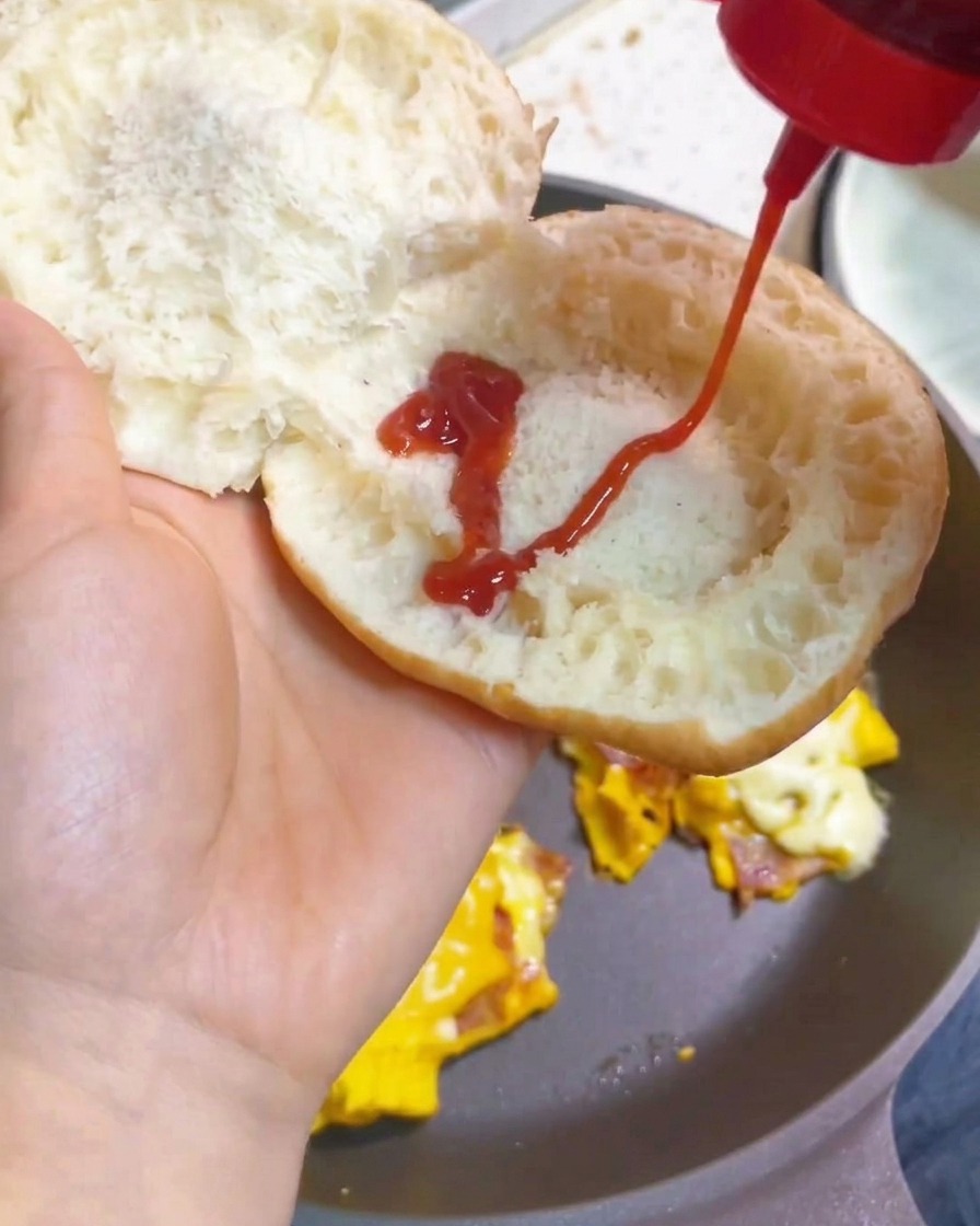 Ręka wyciskająca zygzak z ketchupu na wewnętrzną stronę przypieczonej bułki.