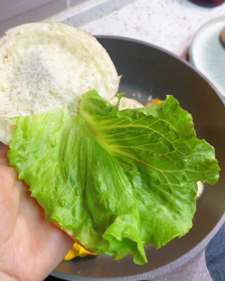 Burger śniadaniowy składany ze świeżą sałatą i usmażonym kotletem jajeczno-bekonowym w bułce.