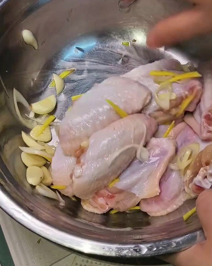 Dłonie mieszające marynowane skrzydełka z aromatami w metalowej misce.