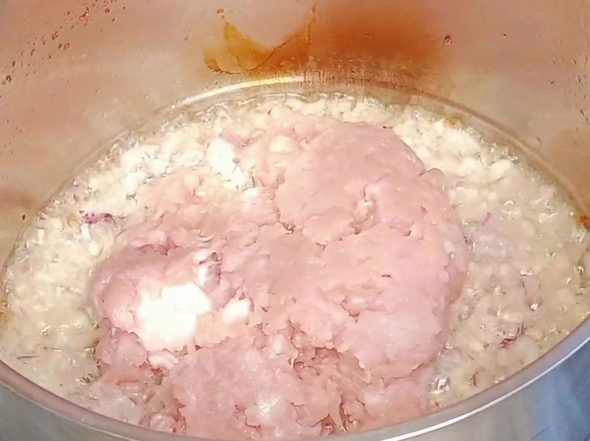 Surowe mięso mielone dodawane do podsmażonej cebuli i czosnku.
