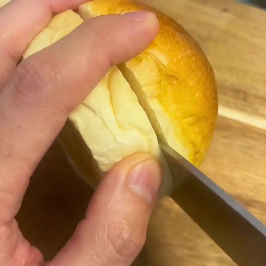 Nóż przekrawający miękką bułkę do burgera na desce do krojenia.