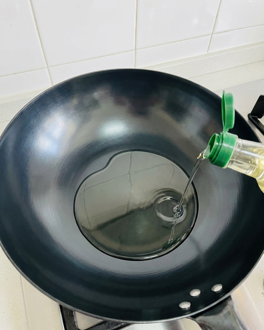 Oliwa z oliwek wlewana do pustego, rozgrzanego ciemnego woka.
