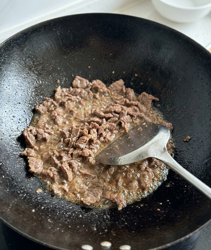 Świeżo pokrojone pomidory dodawane do zrumienionej wołowiny w woku.