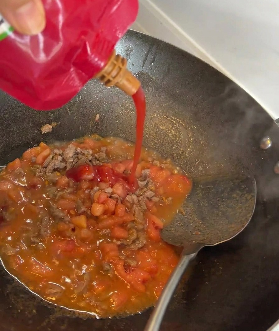 Pasta pomidorowa wlewana do patelni z podsmażaną wołowiną i pomidorami.