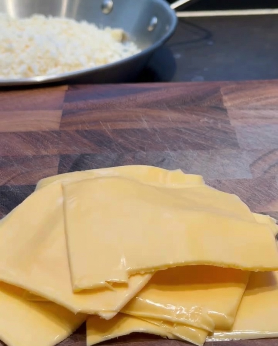 Plastry sera cheddar krojone na mniejsze kawałki na drewnianej desce.