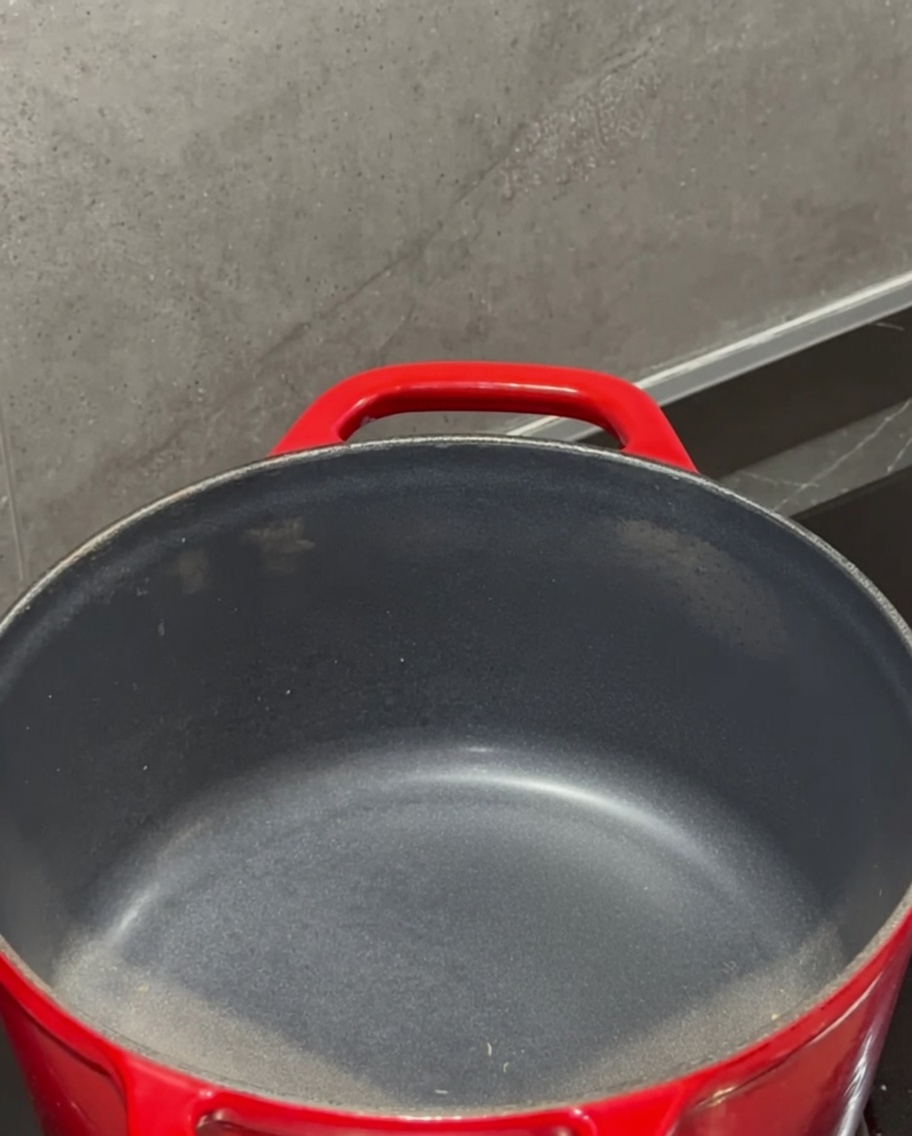 Kostka masła rozpuszczająca się w czerwonym garnku na kuchence.