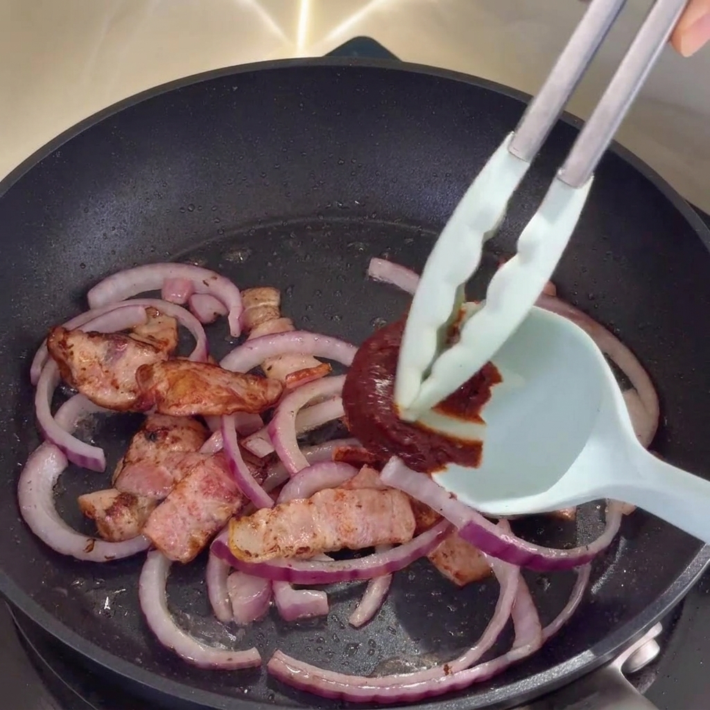Koreańska pasta gochujang mieszana z bekonem i cebulą na patelni.