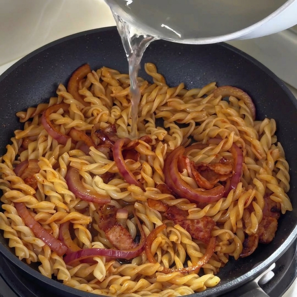 Gorąca woda z gotowania makaronu wlewana na patelnię z fusilli.