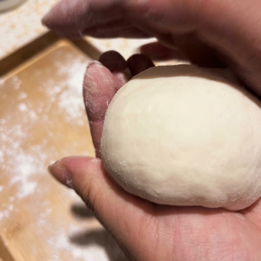 Dłonie kształtujące kawałek surowego ciasta na pizzę w gładką kulkę.