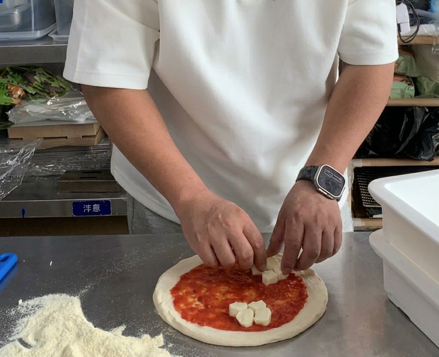 Dłonie układające kawałki świeżej mozzarelli na pizzy pokrytej sosem pomidorowym.