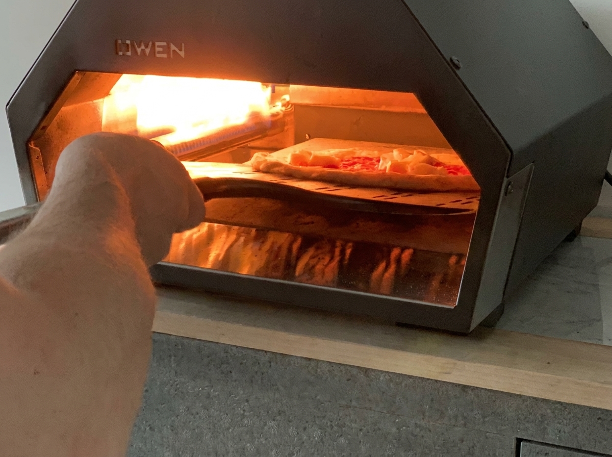 Łopata wsuwająca surową pizzę do gorącego gazowego pieca do pizzy.
