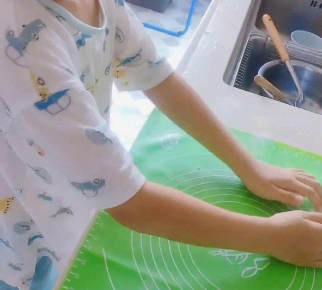 Kula ciasta na pizzę wyrabiana na zielonej silikonowej macie.