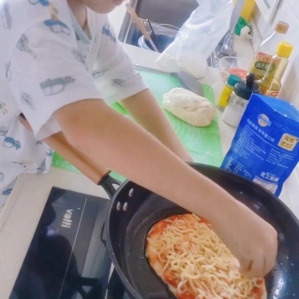 Zbliżenie na spód pizzy na patelni posypywany grubą warstwą tartej mozzarelli.