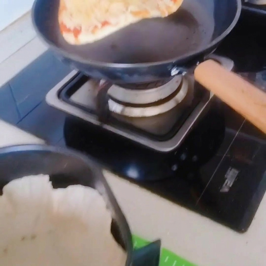 Pizza ostrożnie przekładana z patelni do kosza air fryera wyłożonego papierem do pieczenia.