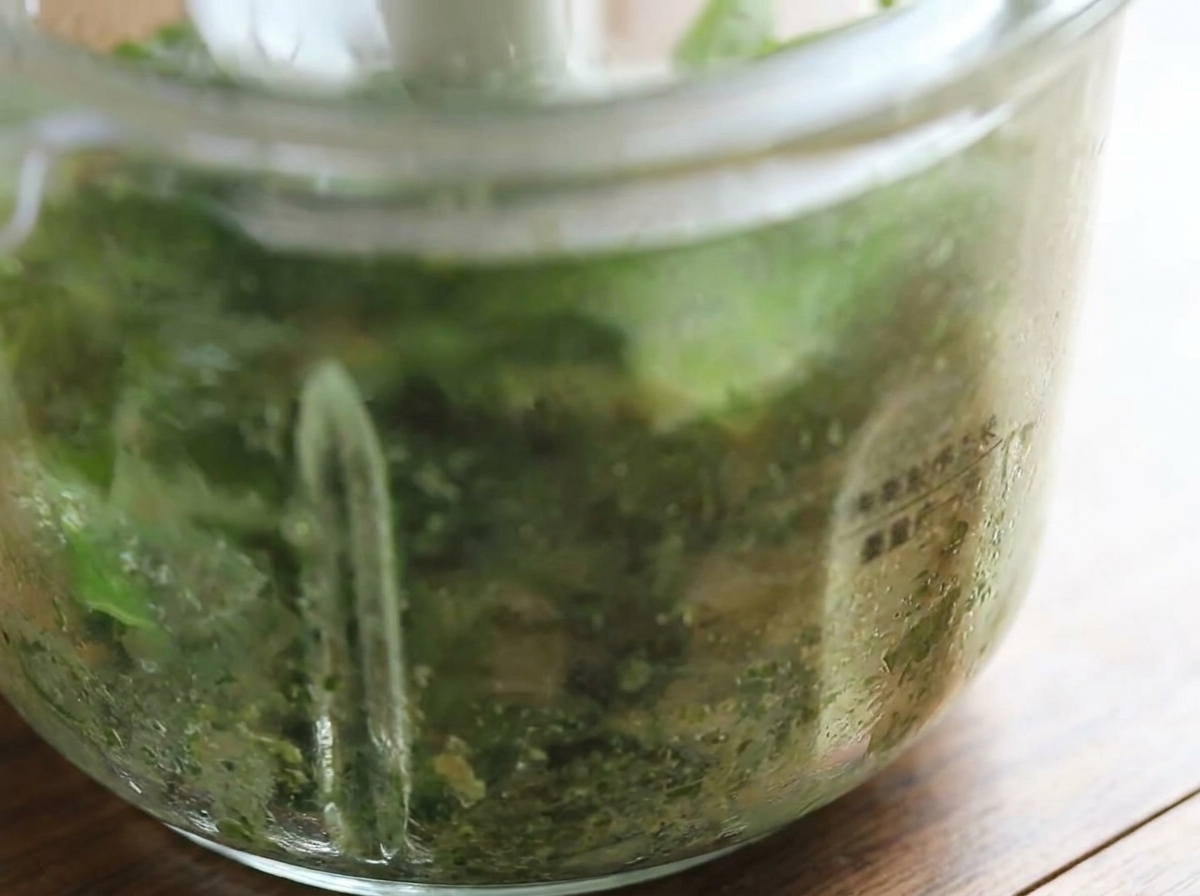 Zbliżenie na misę robota kuchennego pokazujące świeżo zmielone, jasnozielone pesto bazyliowe.