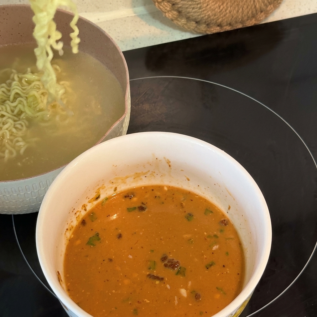 Ugotowany, kręcony makaron ramen jest podnoszony i przenoszony do miski wypełnionej kremowym bulionem.