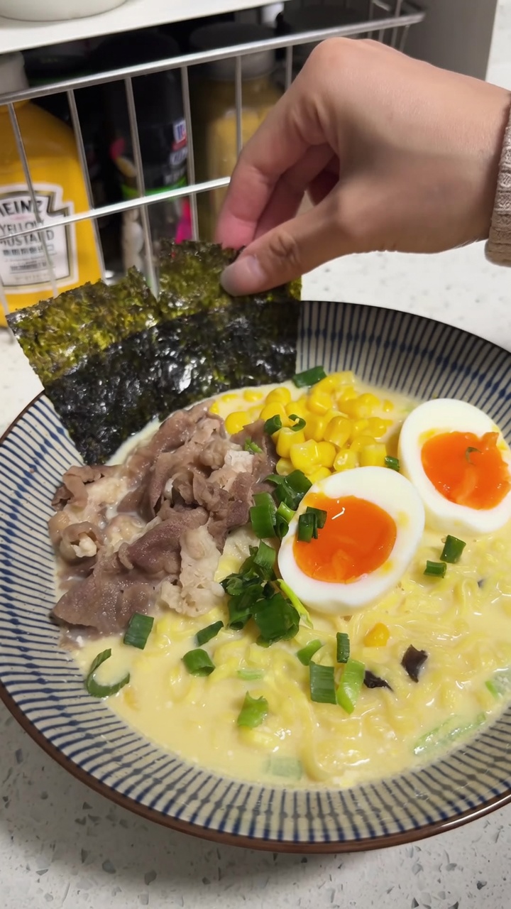 Kremowa miska ramenu instant w stylu Tonkotsu z dodatkiem wołowiny, kukurydzy, jajek na miękko i świeżej dymki.
