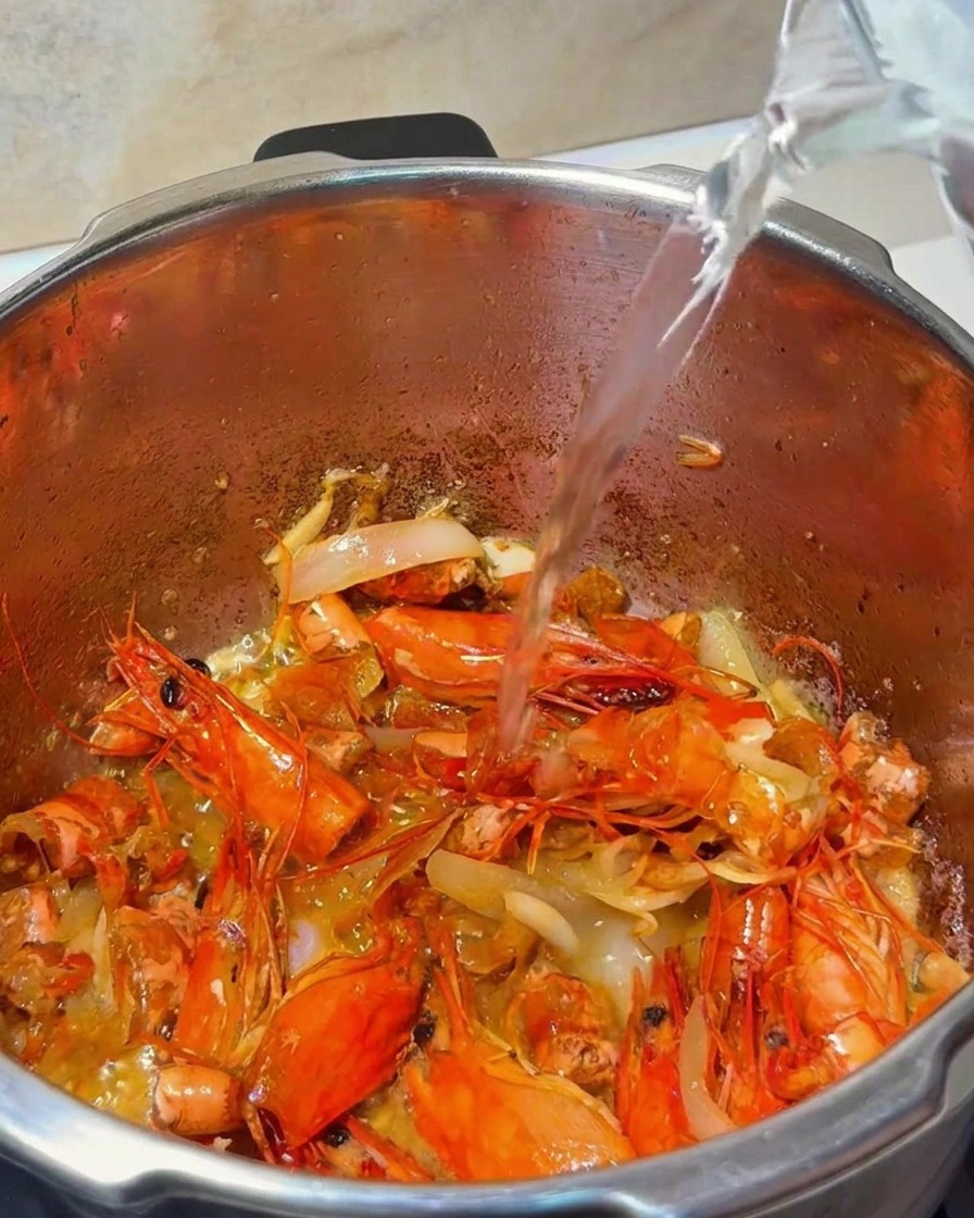 Woda wlewana z dzbanka do garnka zawierającego skorupki krewetek i aromaty.