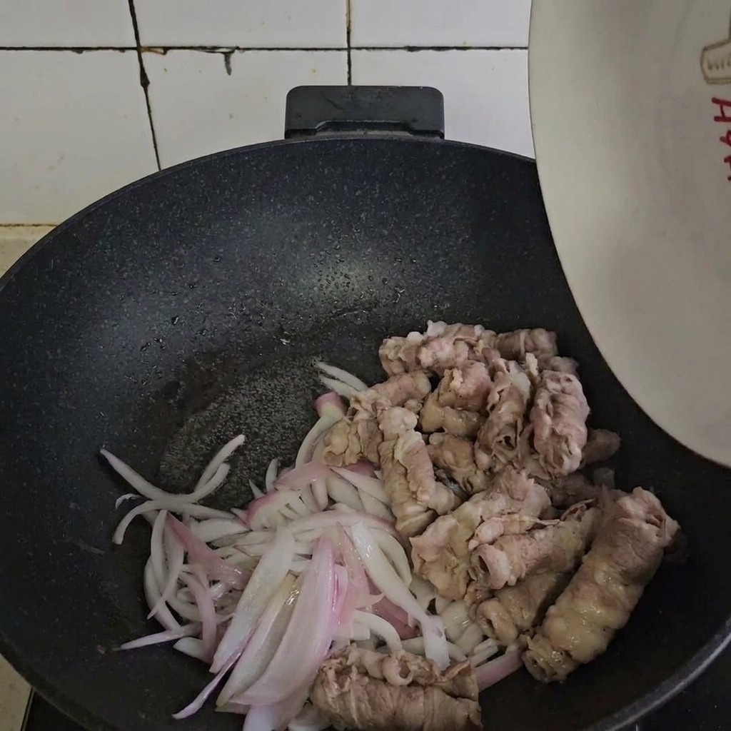 Zblanszowana wołowina dodawana do podsmażonej cebuli na patelni.