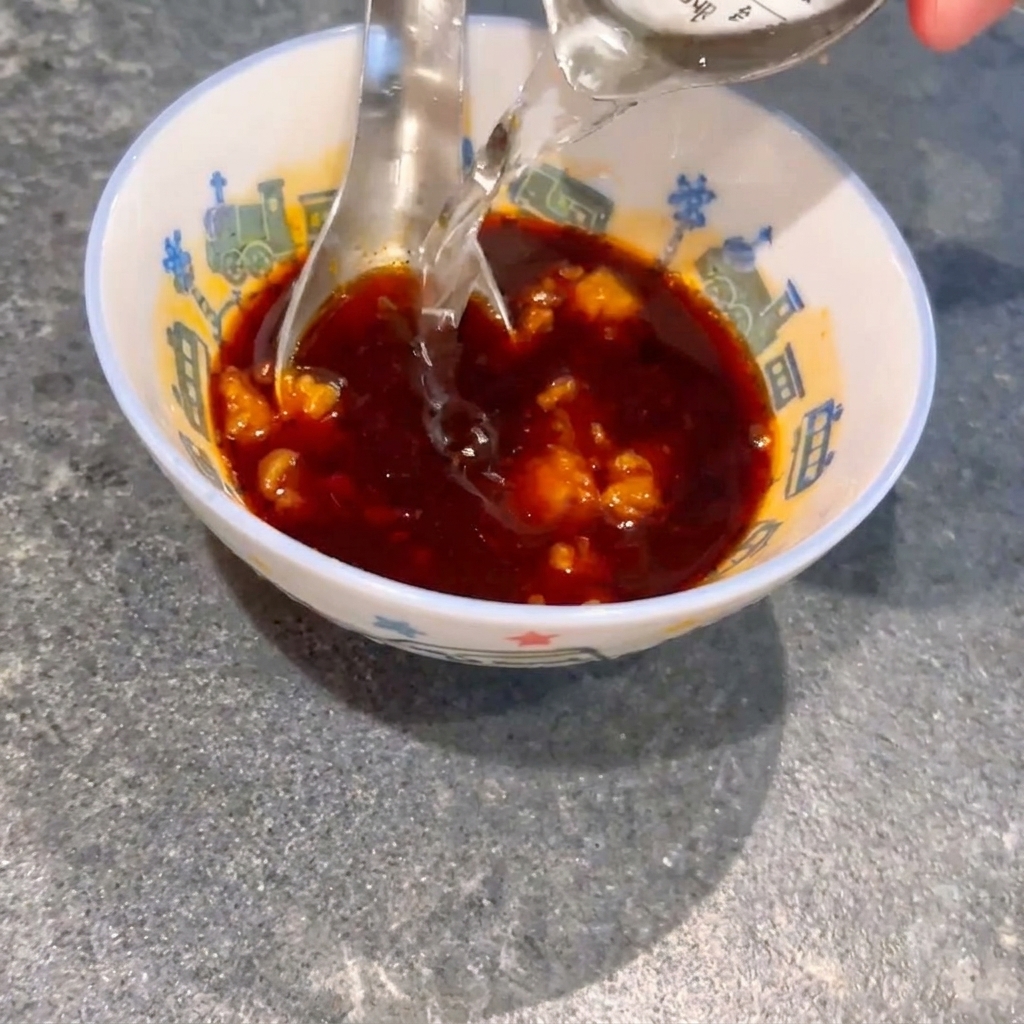 Woda wlewana do małej miseczki z ciemnym sosem sojowym i grudkami miso, podczas gdy łyżka miesza całość.