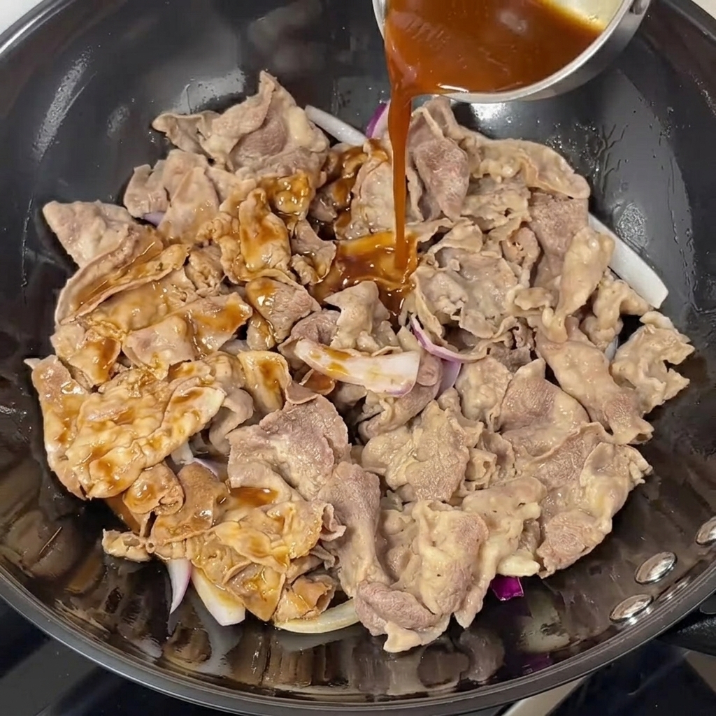 Ciemny sos teriyaki wlany na wołowinę z cebulą w woku.