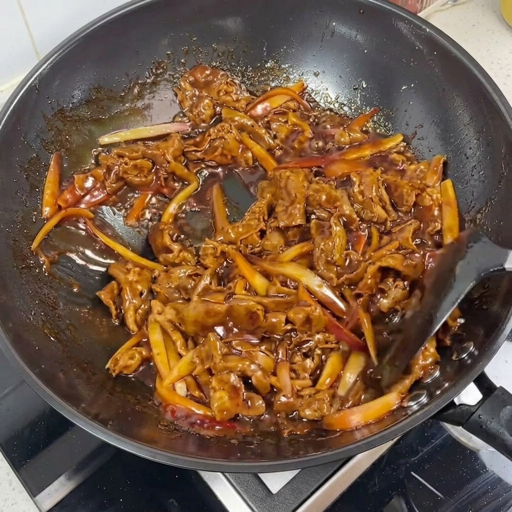Zbliżenie na błyszczące plastry wołowiny i cebuli w sosie teriyaki.