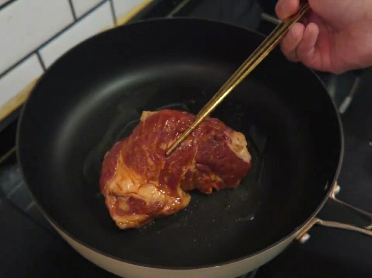 Surowy marynowany kotlet układany na rozgrzanej patelni z olejem.