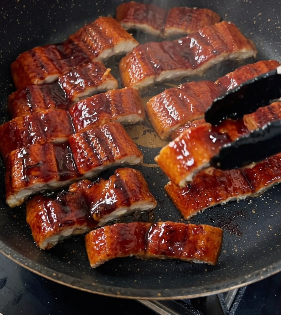Kawałki grillowanego węgorza glazurowane na patelni w gęstym ciemnym sosie.