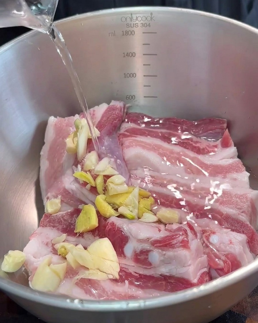 Miska z paskami boczku przyprawianymi posiekanymi aromatami i czerwoną sfermentowaną pastą sojową.