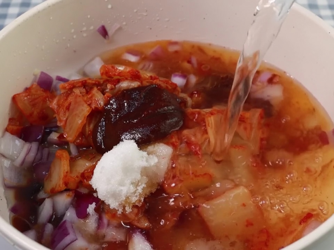 Woda wlewana do garnka z bazą z kimchi i przypraw.