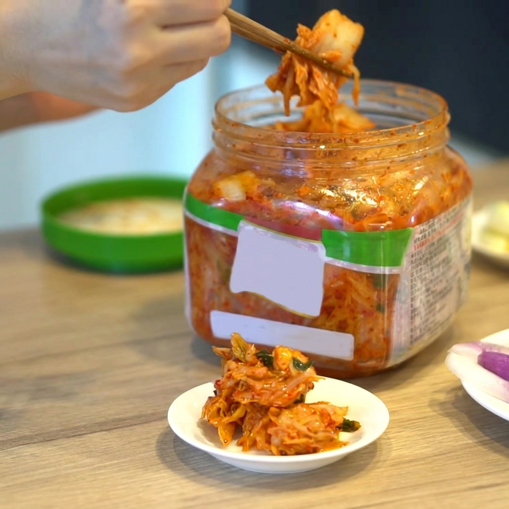 Porcja koreańskiego kimchi wyjmowana z pojemnika pałeczkami.