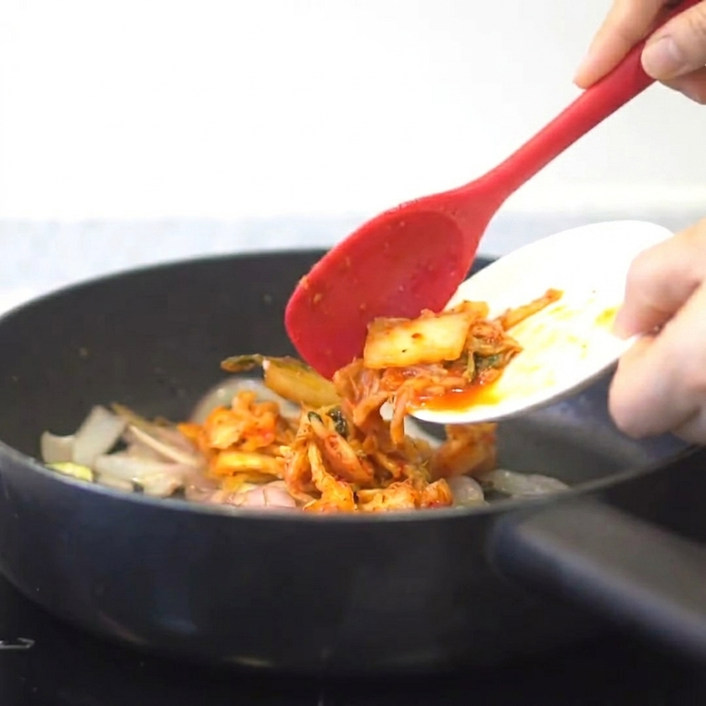 Kimchi dodawane do patelni z podsmażoną cebulą i czosnkiem.